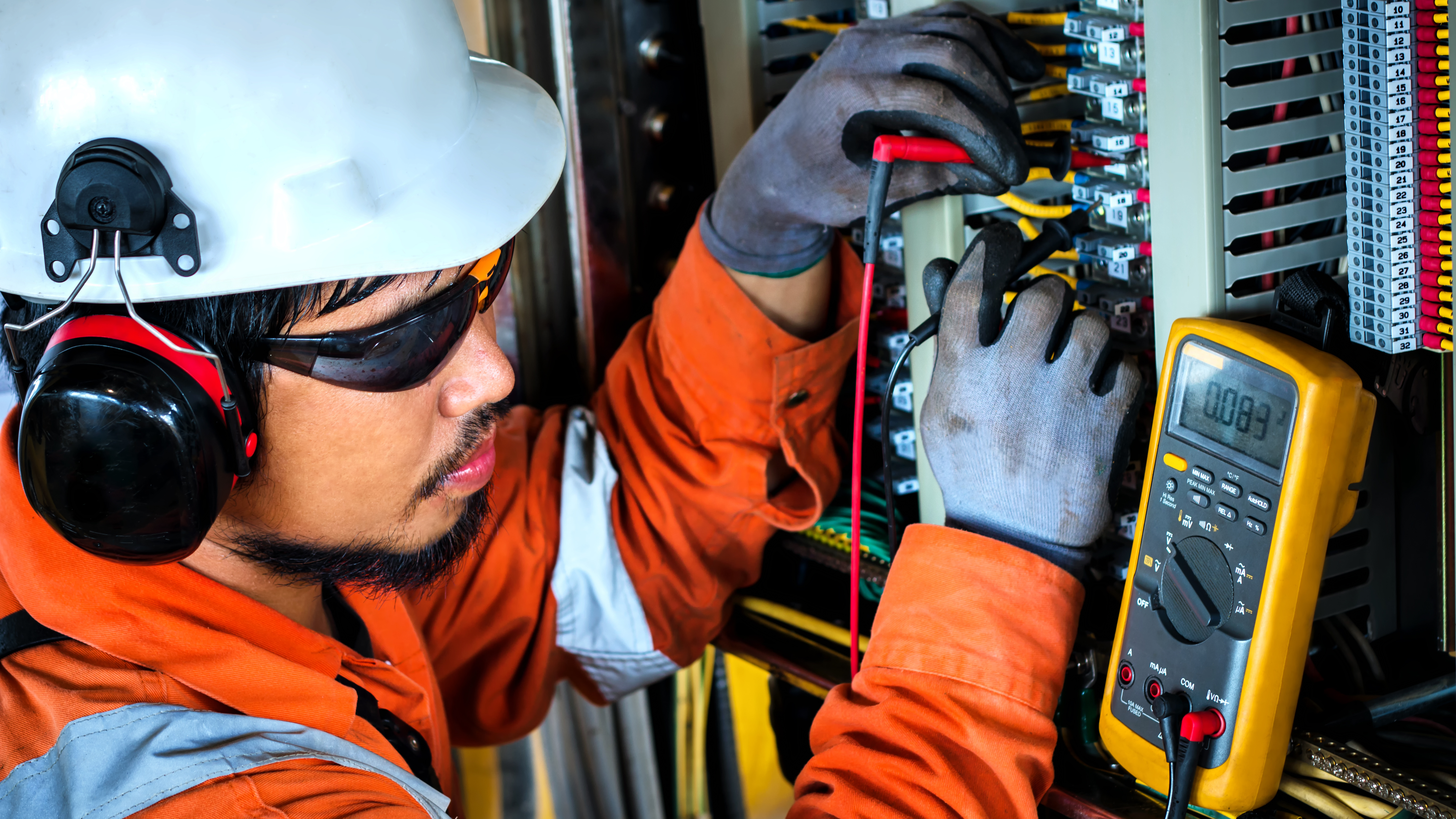  Dynamo technician using a multimeter to test panel during plant shutdown.  The employee is wearing Personal Protective safety equipment consisting of hardhat, ear protection and safety glasses.