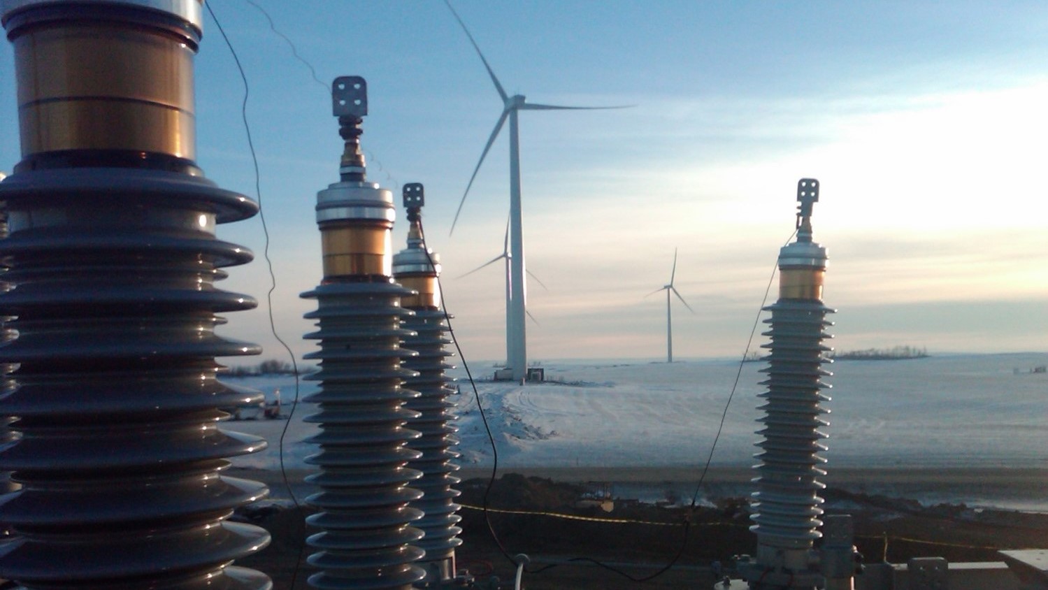 Electrical insulators with wind turbines in the background. This was one of Dynamo's past projects. The location is a wind farm with a beautiful skyline.
