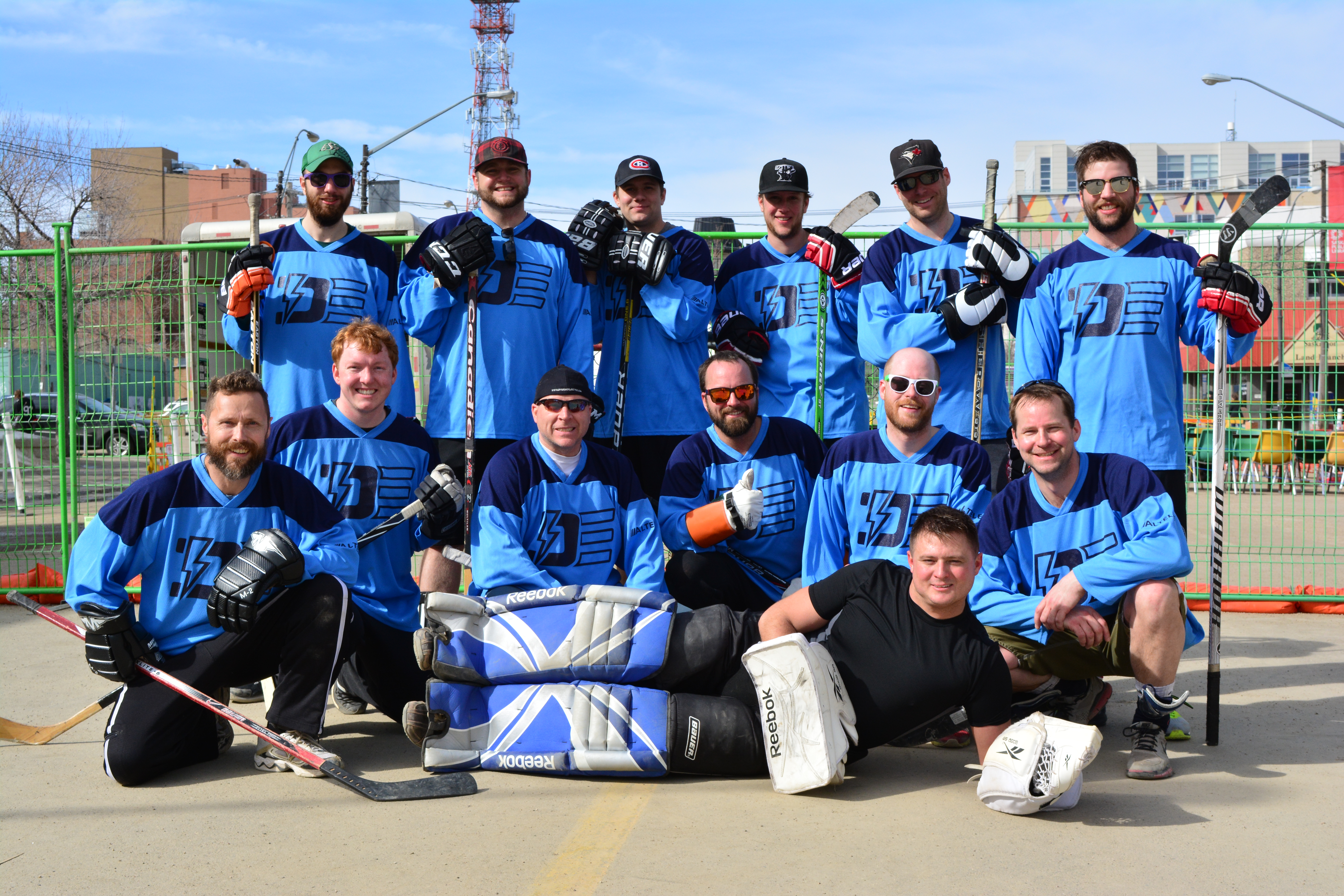 Group photo of the Dynamo employee's road hockey team. All are wearing hockey gloves, holding sticks and wearing Dynamo hockey jerseys.