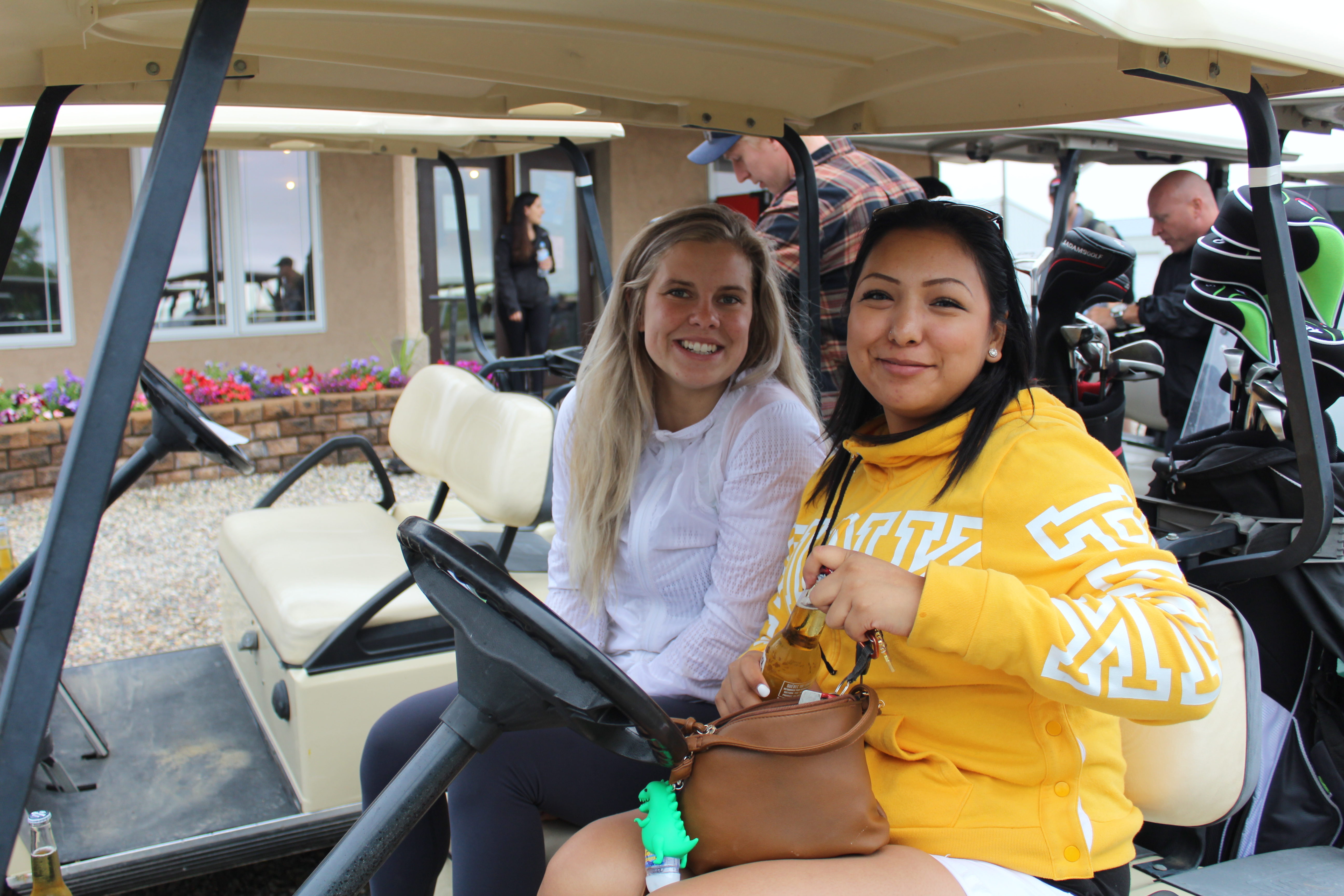 Two female Dynamo employees are posing for a photo in a golf cart as they get ready for the dynamo golf tournament. 