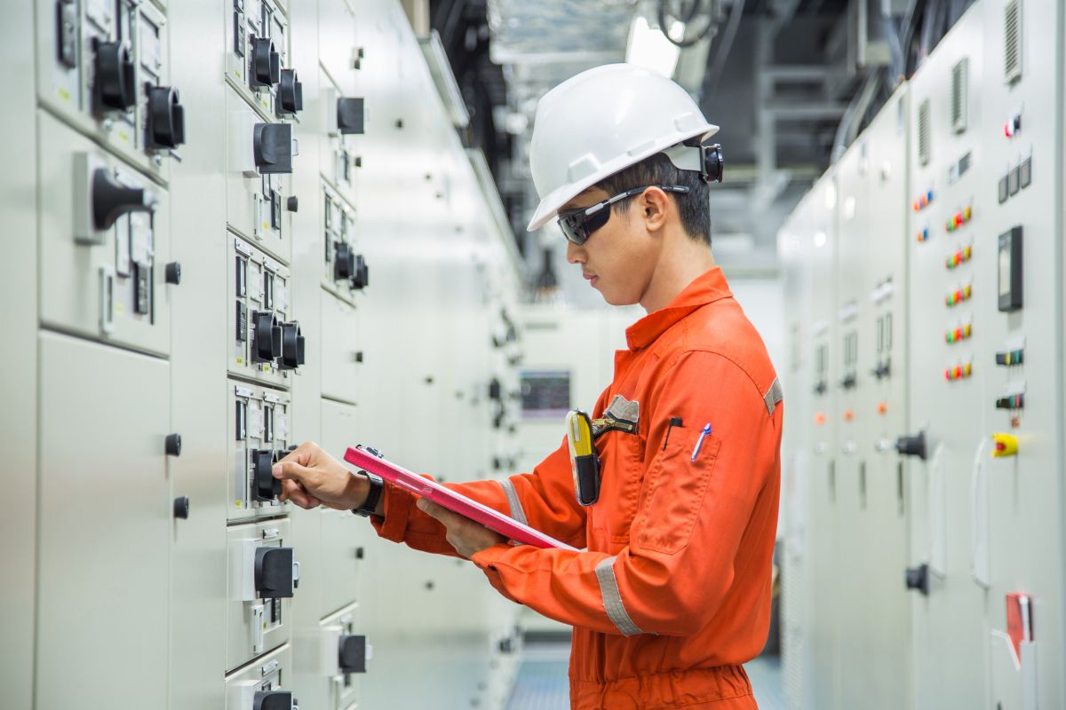  Dynamo employee doing maintenance testing on the control panel to minimize risk to person and equipment. The employee is in coveralls and is wearing a hard hat and protective eyewear.