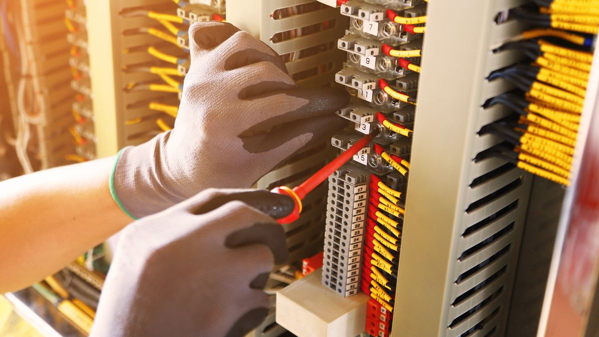  A shot of a Dynamo technician gloved hands using a screw to remove a wire from the control panel.  