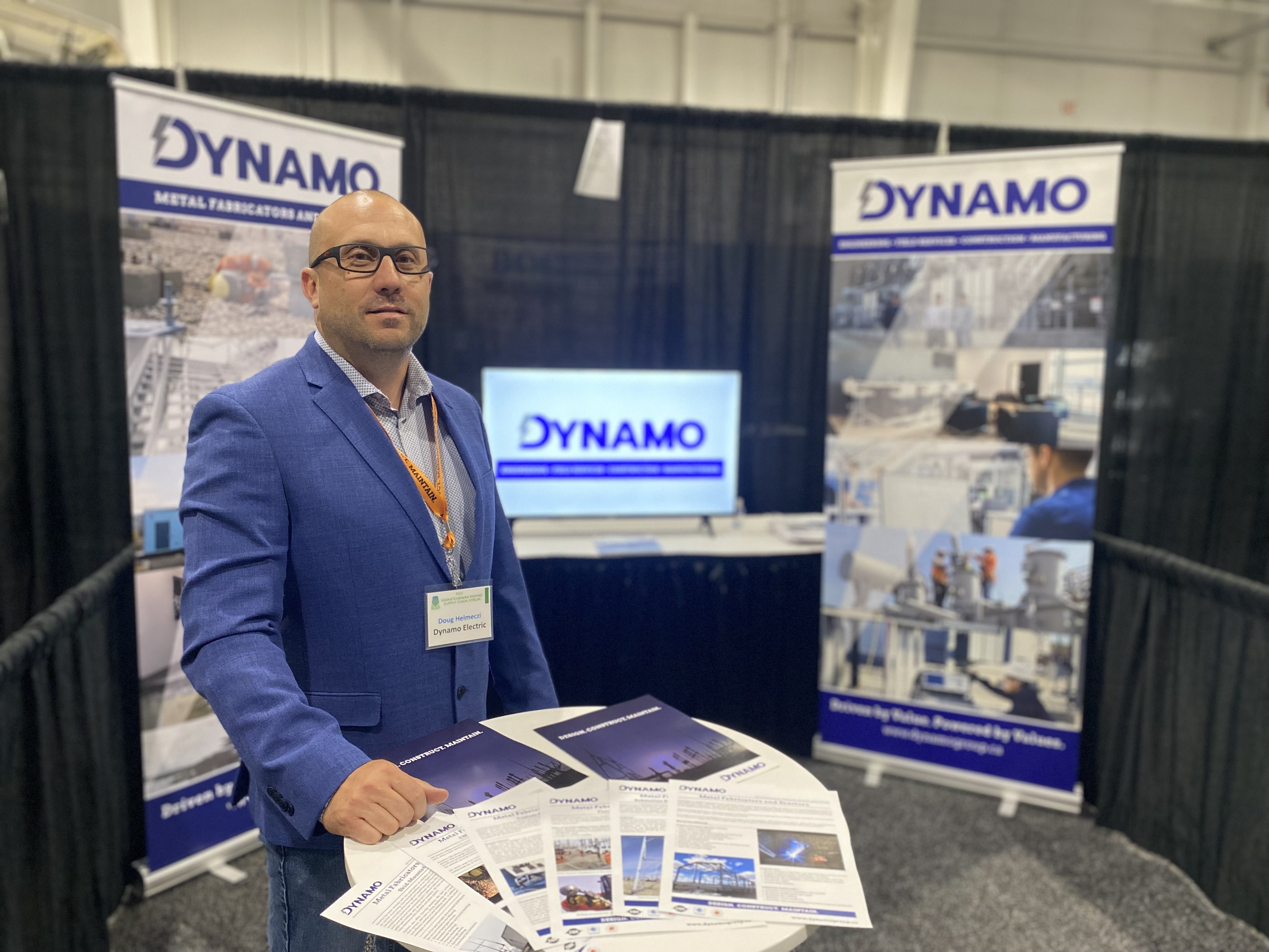 Doug Helmeczi at the Saskatchewan Mining Supply Chain Forum standing in front of the Dynamo boothh